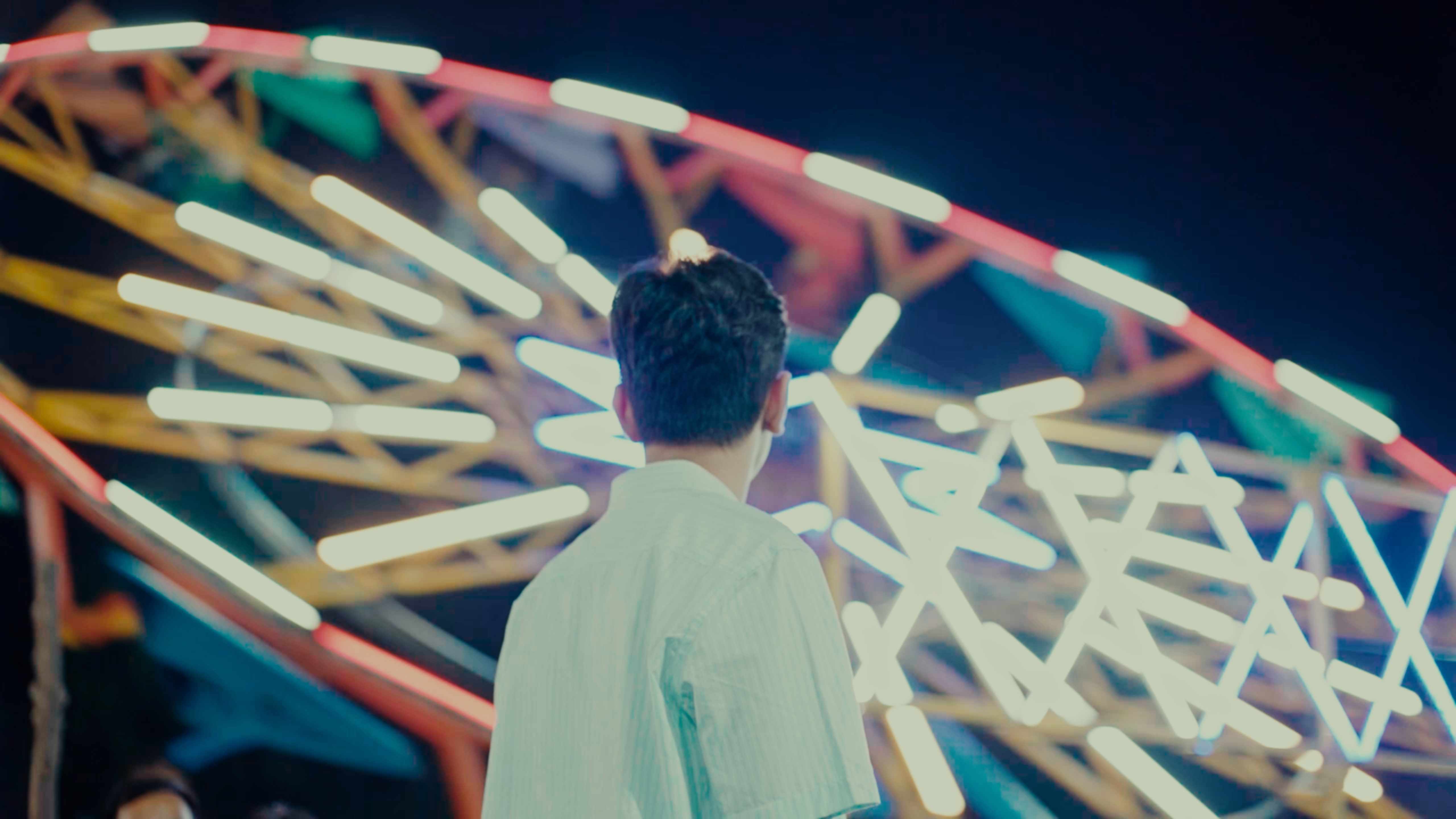 Young man looking at a colorful carnival ferris wheel at night